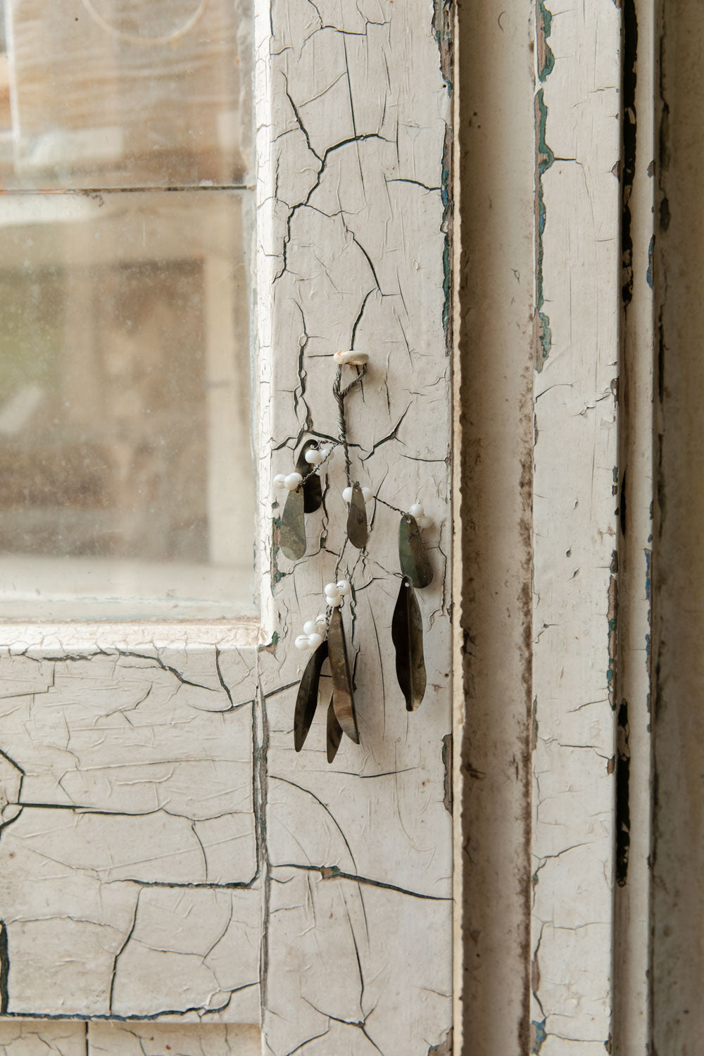 Small bunch of antiqued silver mistletoe with white beads hanging against cracked white paint