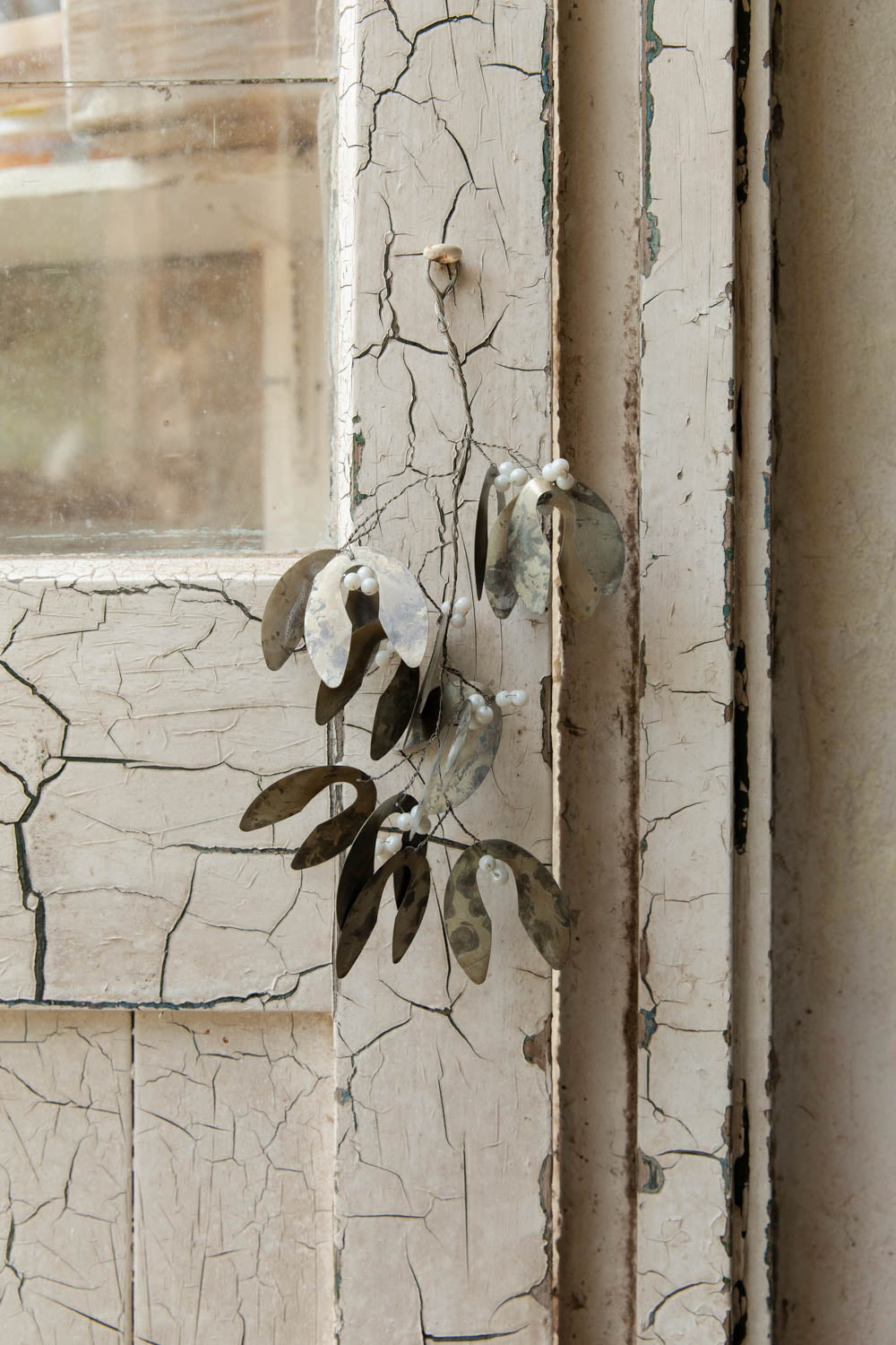 Full antiqued silver mistletoe with white beads hanging on a weathered painted door frame