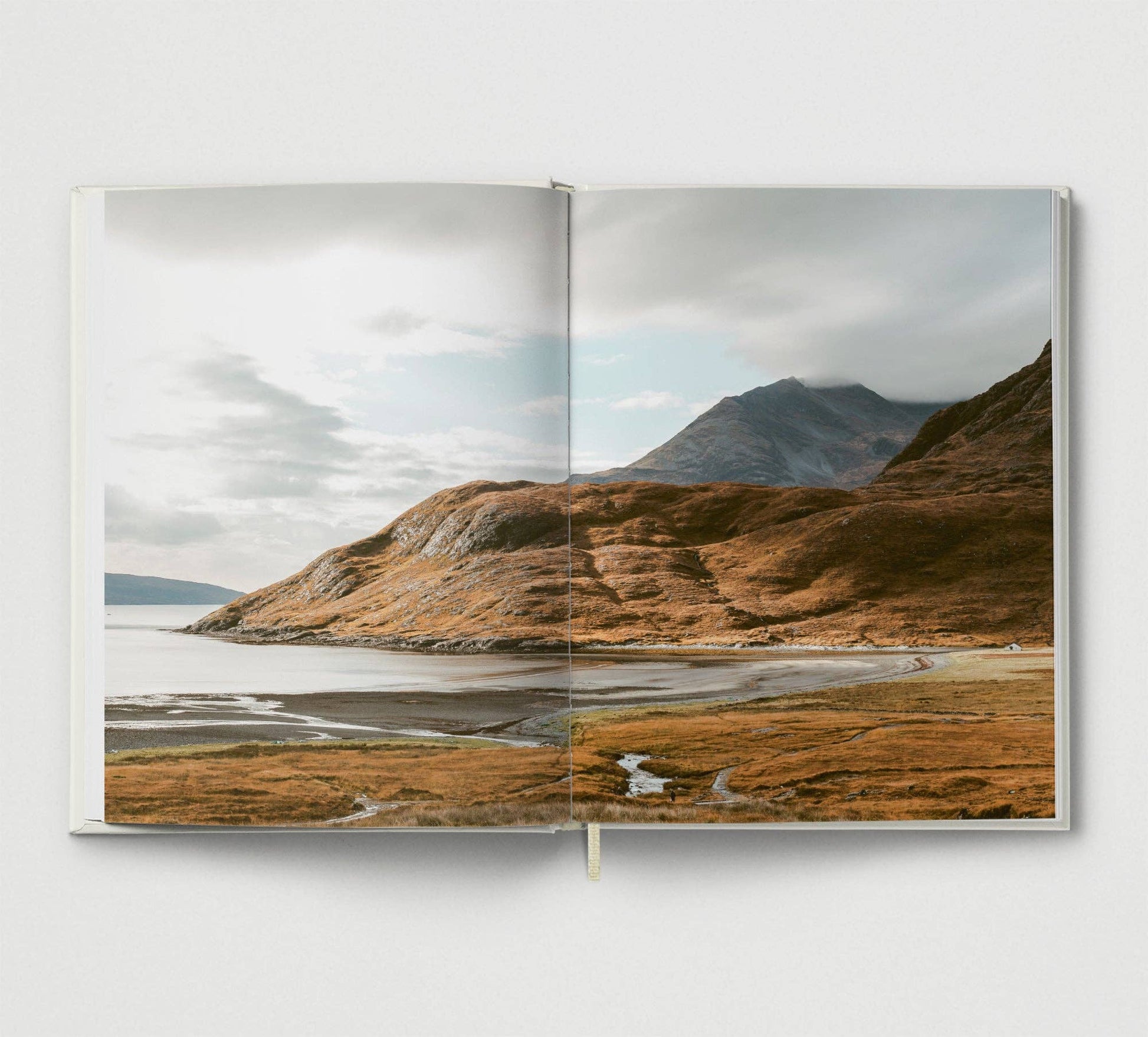 Open book showing a landscape with mountains and water on a white background.