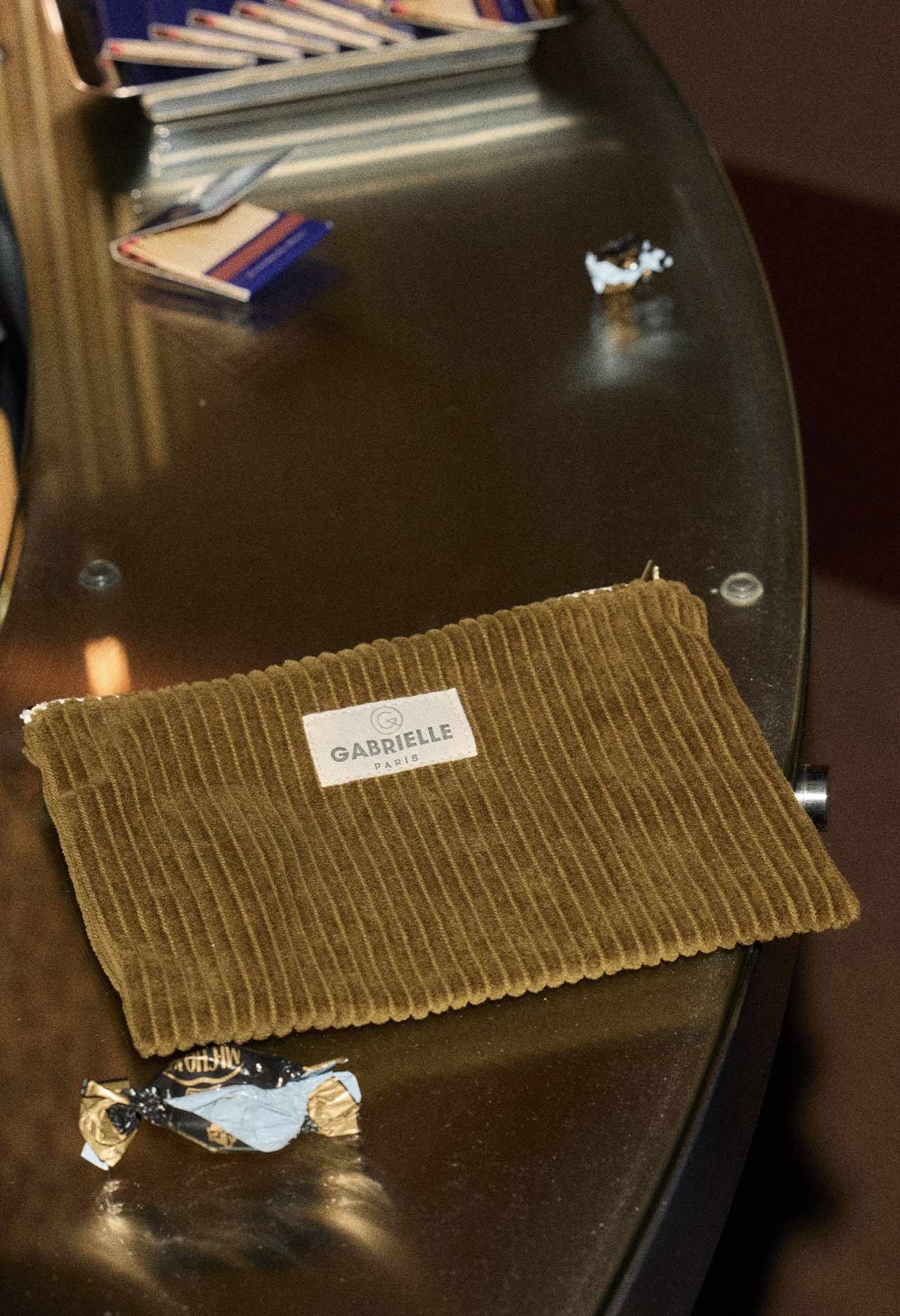 Small olive velvet corduroy pouch sat on a reflective surface.