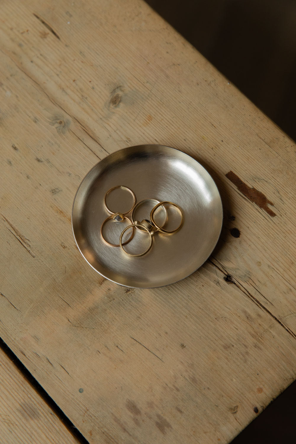 Small round silver plate holding gold rings on a pine table