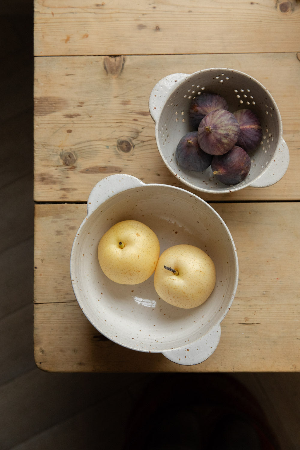 Overhead of white speckle berry bowls filled with figs and golden pears