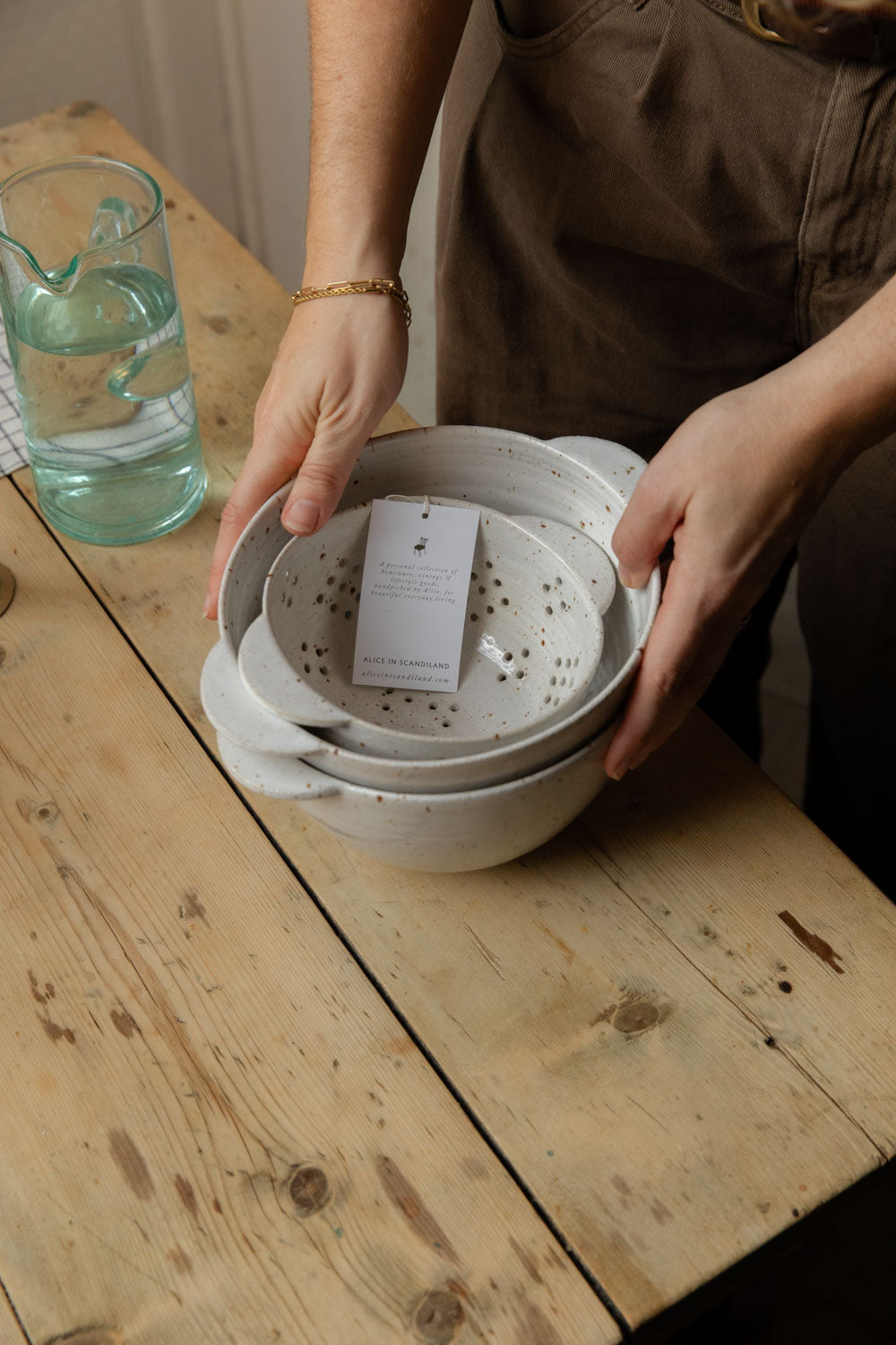 Hands holding a stack of white speckle stoneware berry bowls with swing tag
