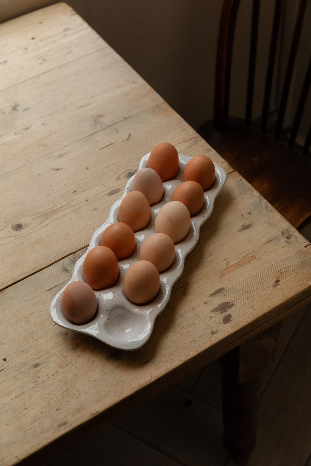 Natural speckle stoneware egg tray of brown eggs on the corner of a farmhouse table