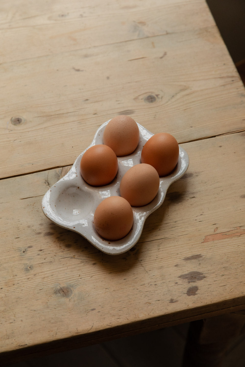 Small speckled stoneware egg tray with five brown eggs on a scrubbed wooden table
