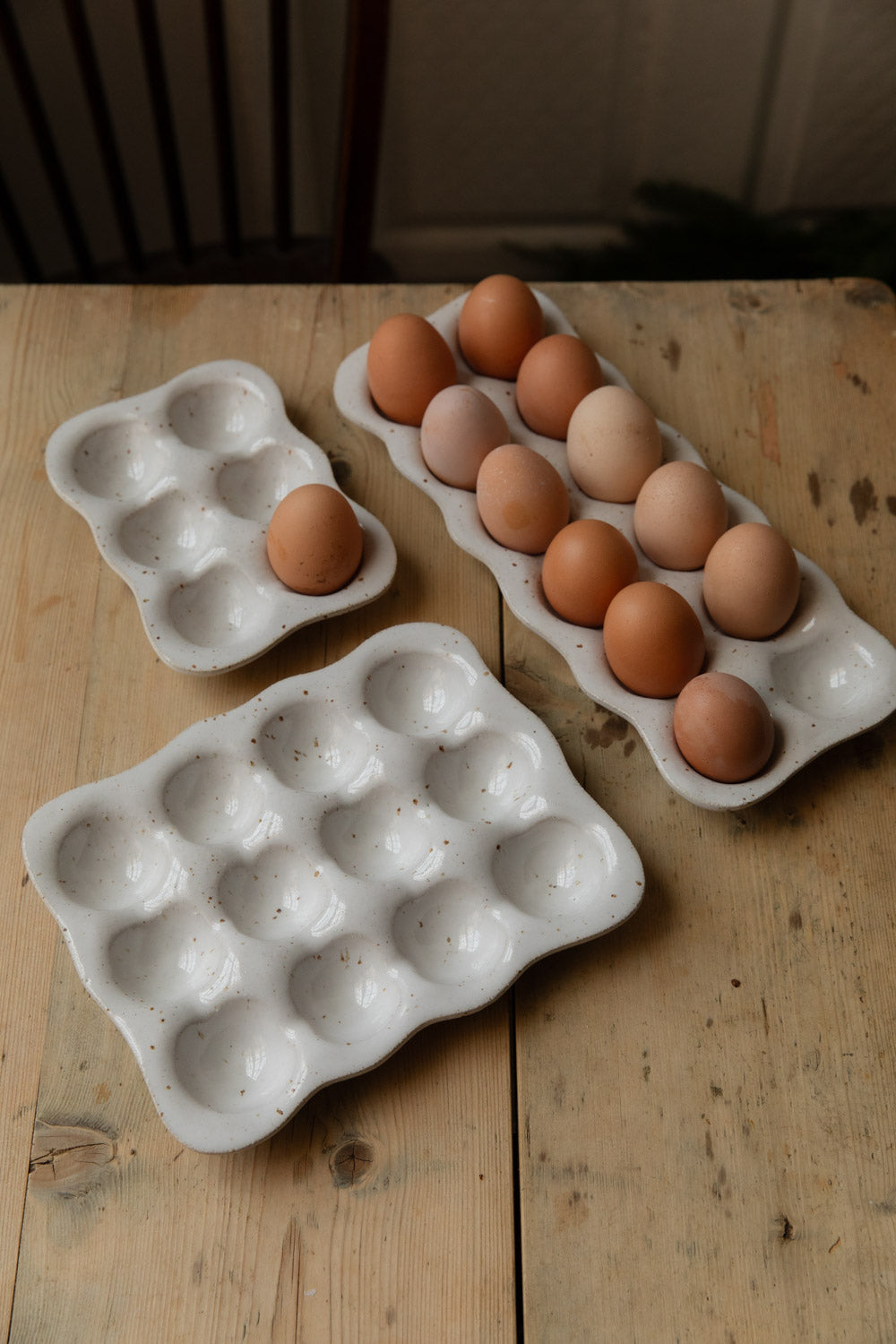Speckled stoneware egg trays, one filled with brown eggs, on a pine table