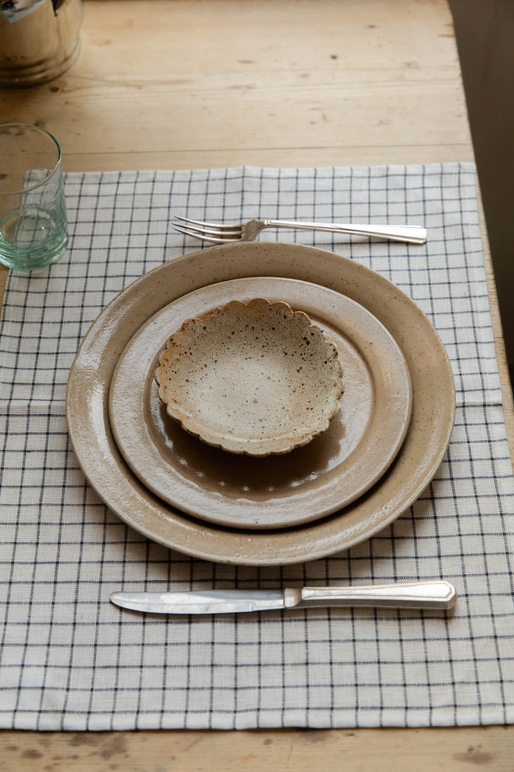 Place setting of speckled stoneware plates and a scalloped dish on a white and black grid Jenn linen placemat