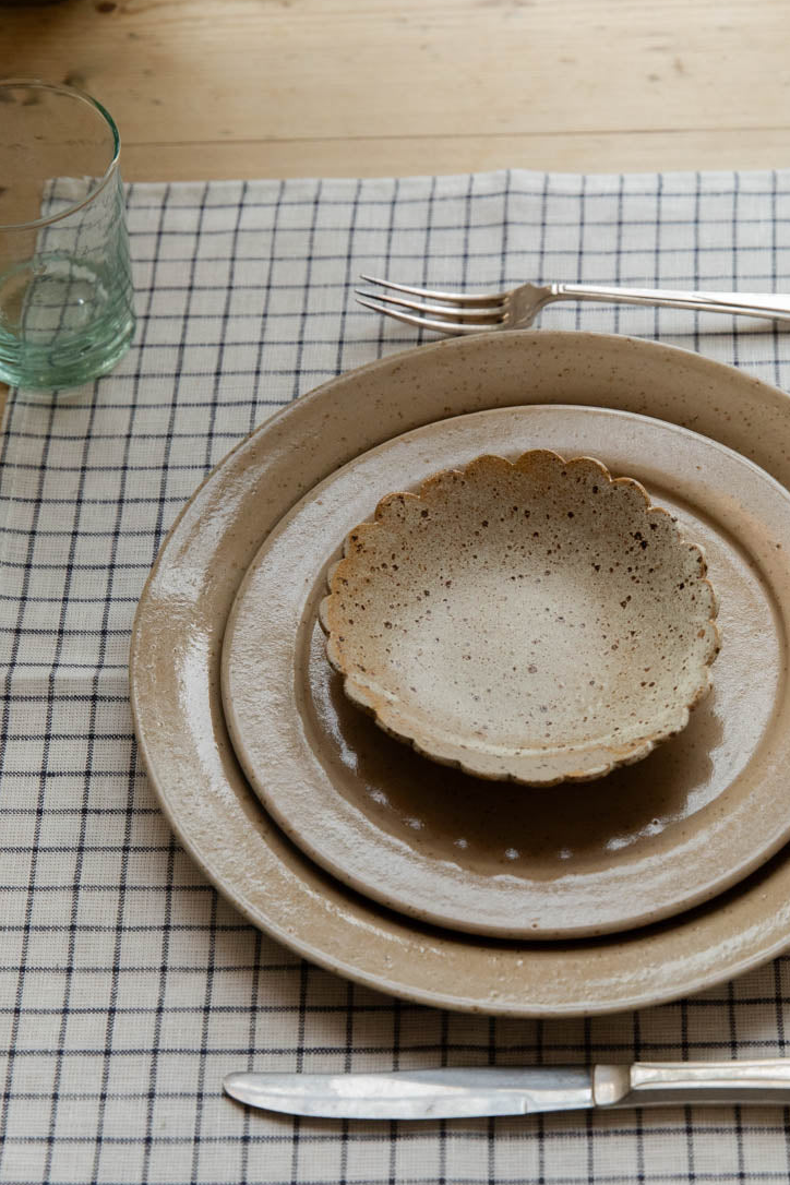 Place setting of speckled stoneware plates and a scalloped dish on a black and white grid napkin