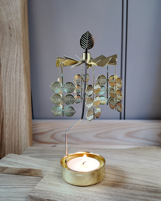 Gold metal Änglaspel tealight carousel featuring Stig Lindberg's Berså leaf pattern, spinning above a lit tealight on a wooden surface