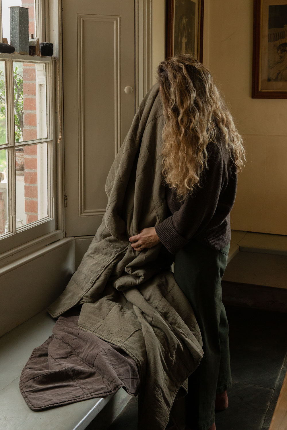 Woman sitting on a window seat wrapped in a eucalyptus green stonewashed cotton quilt