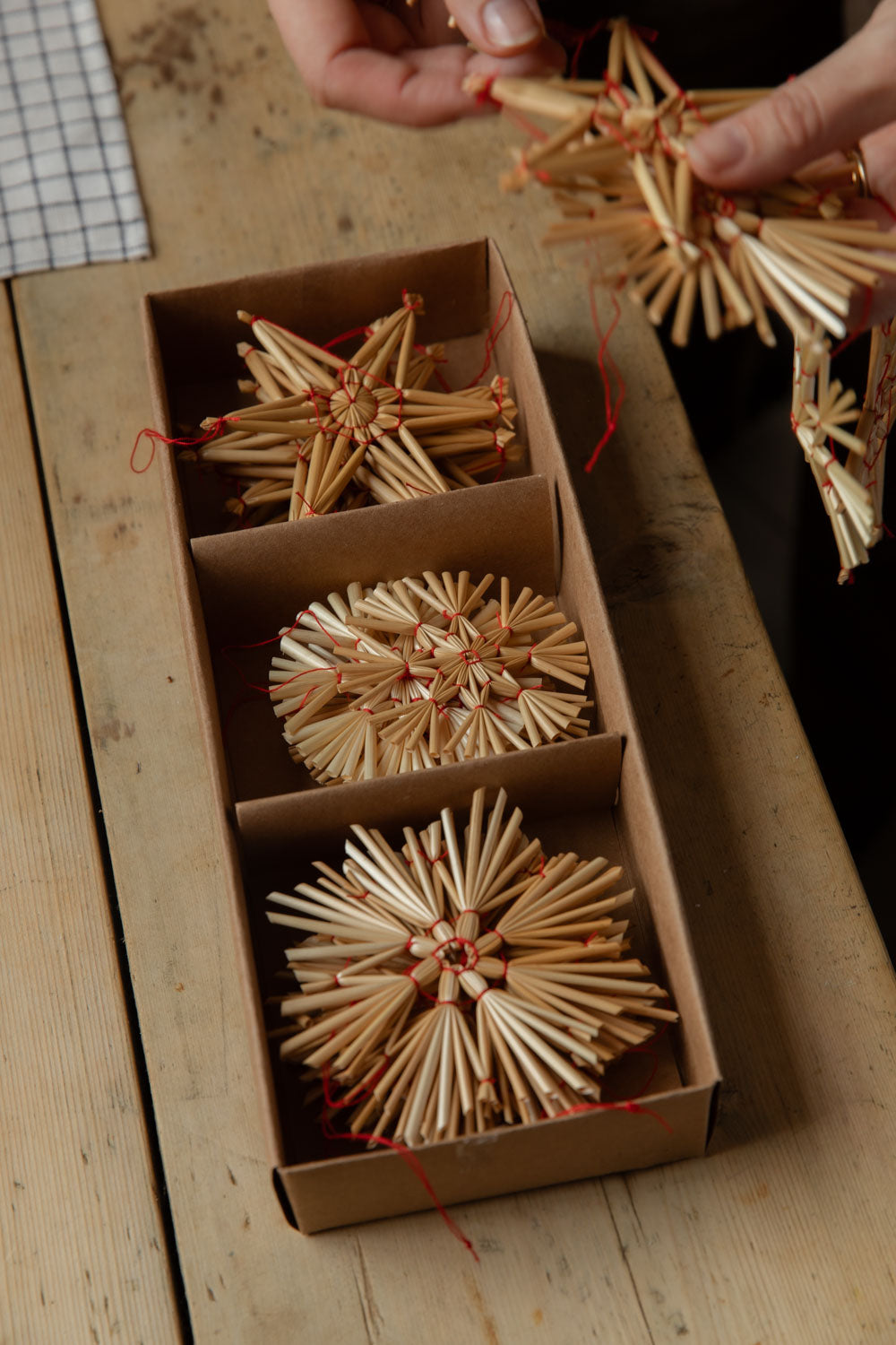 Box of handmade straw star Christmas decorations with a hand lifting one out