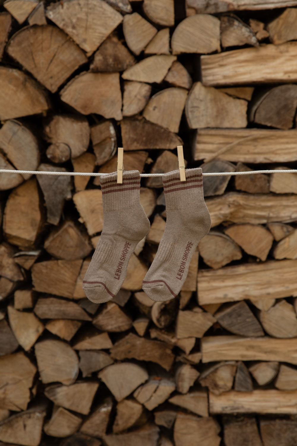 Le Bon Shoppe Girlfriend Socks in Hazelwood, taupe with brown stripes, pegged against firewood