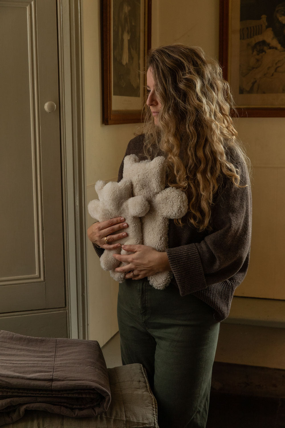 Woman hugging an armful of cream teddy sheepskin hot water bottles in a panelled room