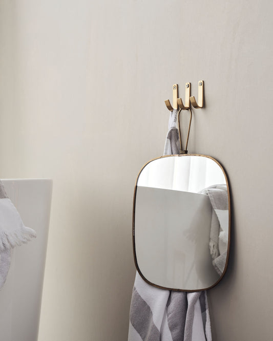 Small rectangular mirror with gold frame on a beige wall, with three brushed brass hooks.