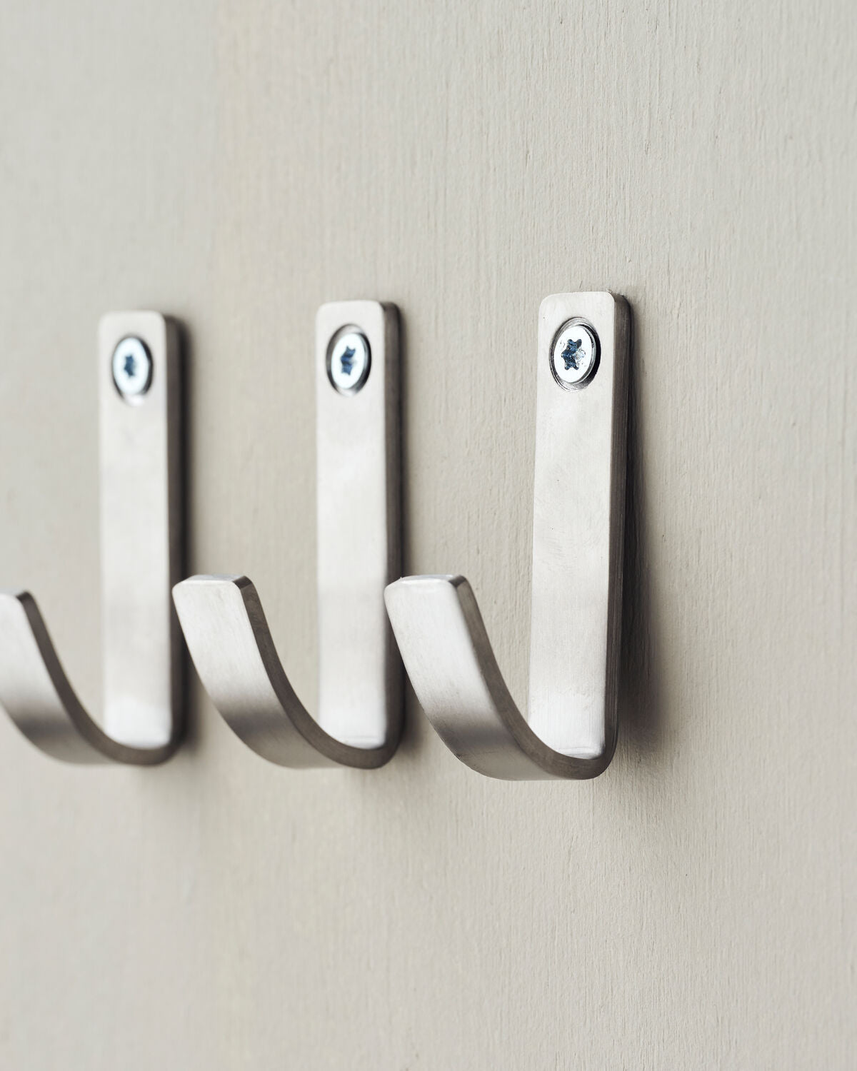 Set of three silver wall hooks on a beige wall.