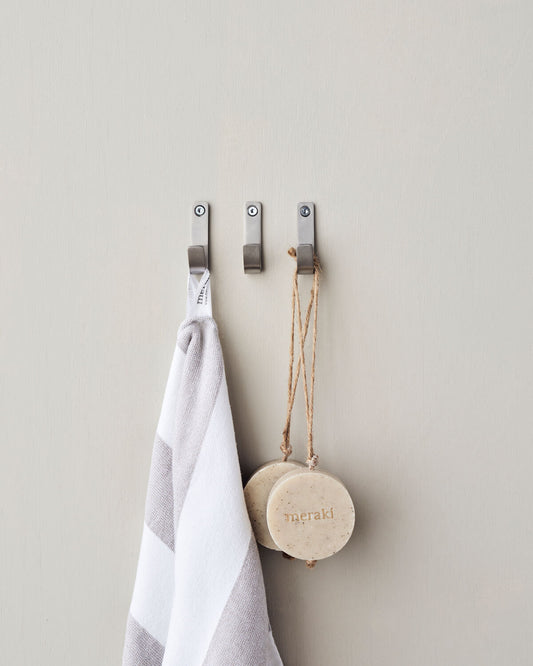Three silver hooks on a wall with a towel and hanging soap.