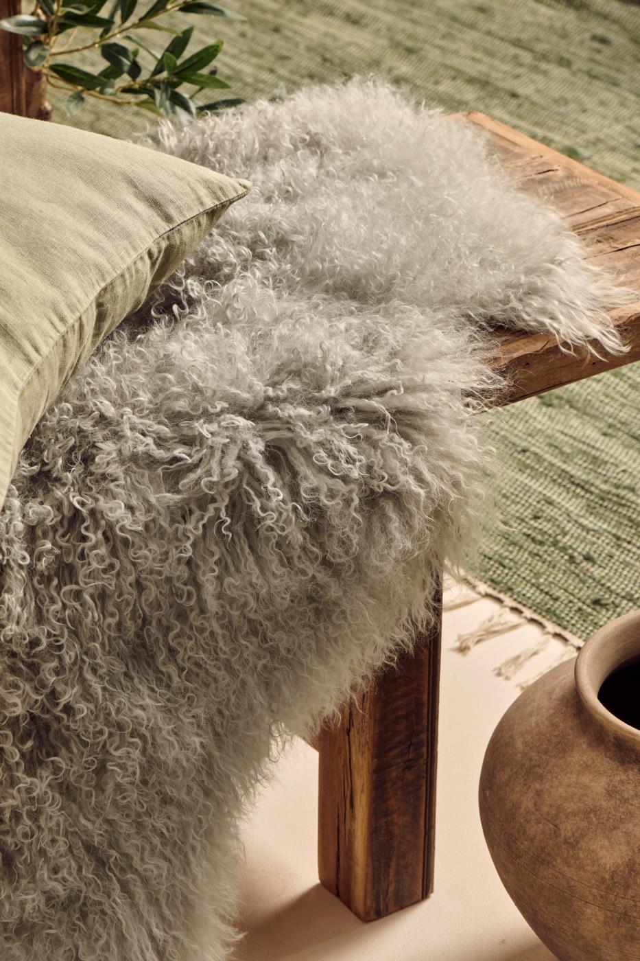 Tibetan sheepskin rug on a wooden surface with a plant and vase in the background.