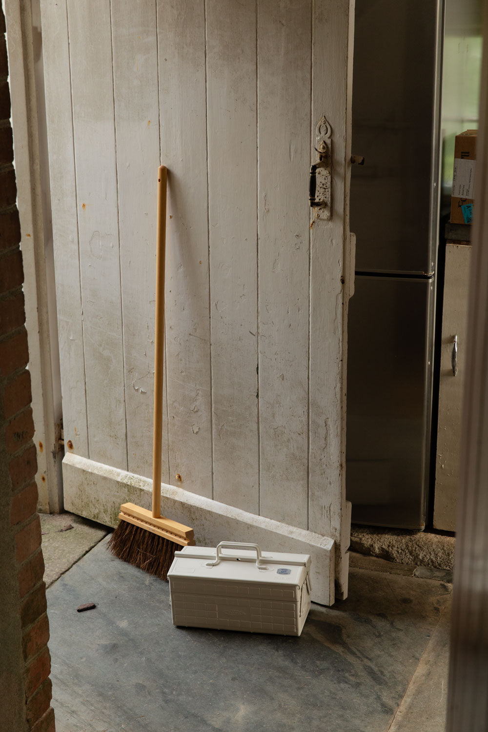 White Toyo toolbox and a long-handled wooden broom by a painted plank door