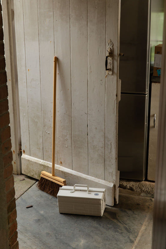 White Toyo toolbox and a long-handled wooden broom by a painted plank door
