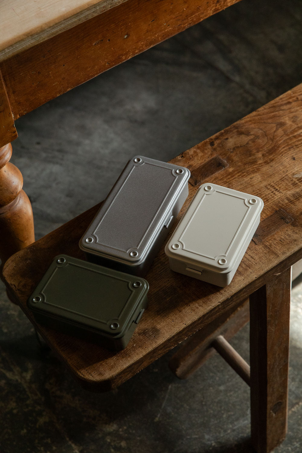 Three small flat Toyo steel boxes in olive, grey and beige on a bench