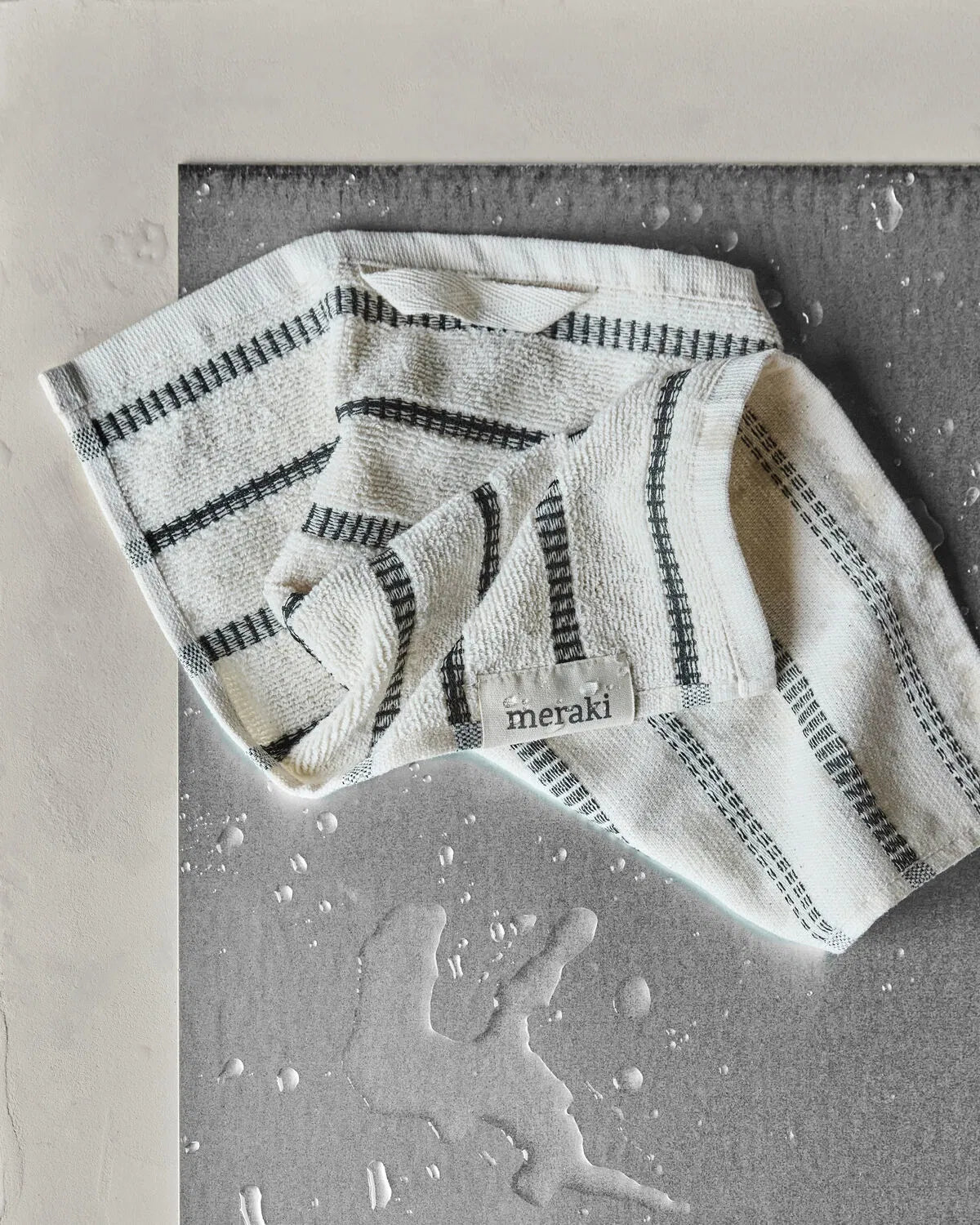 A striped off-white and black washcloth is laying haphazardly on a table, close to a pile of spilt water. 