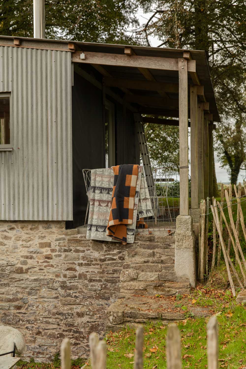 Two wool blankets, a grey and pink Tulip design and an orange block check, hung over a cabin veranda rail