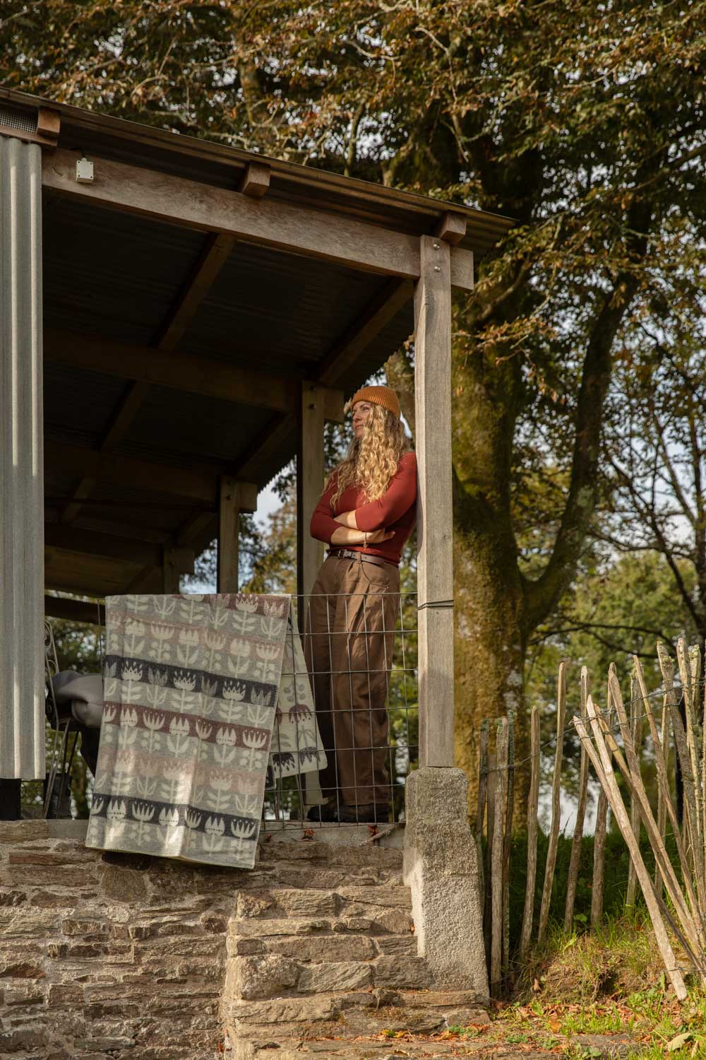 Klippan Tulip lambswool blanket in grey, dusty pink and cream hung over a cabin veranda rail on an autumn afternoon