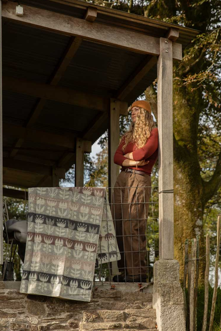 Klippan Tulip lambswool blanket in grey, dusty pink and cream hung over a cabin veranda rail on an autumn afternoon