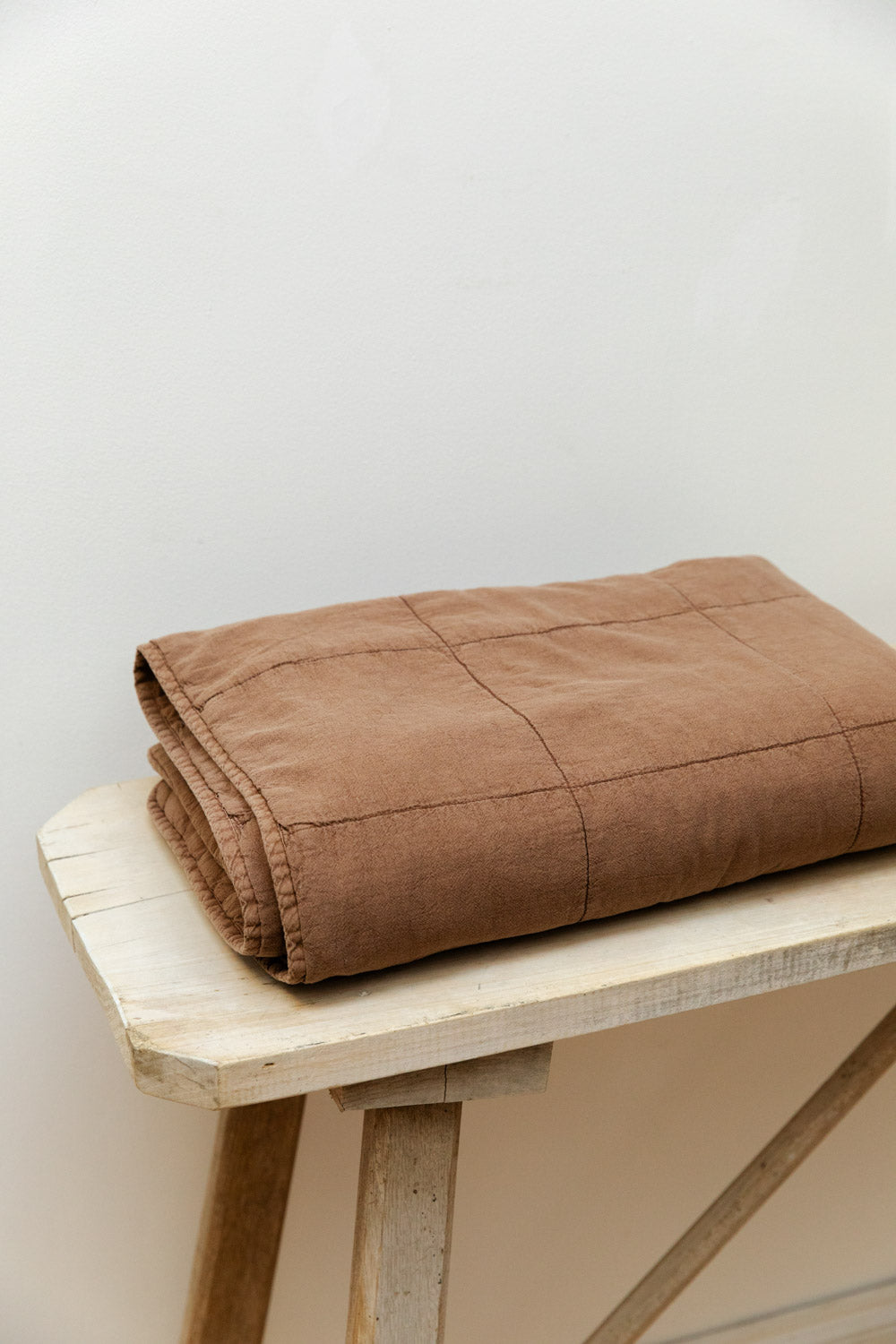 Vintage camel cotton quilt folded neatly on a rustic pale wood table.