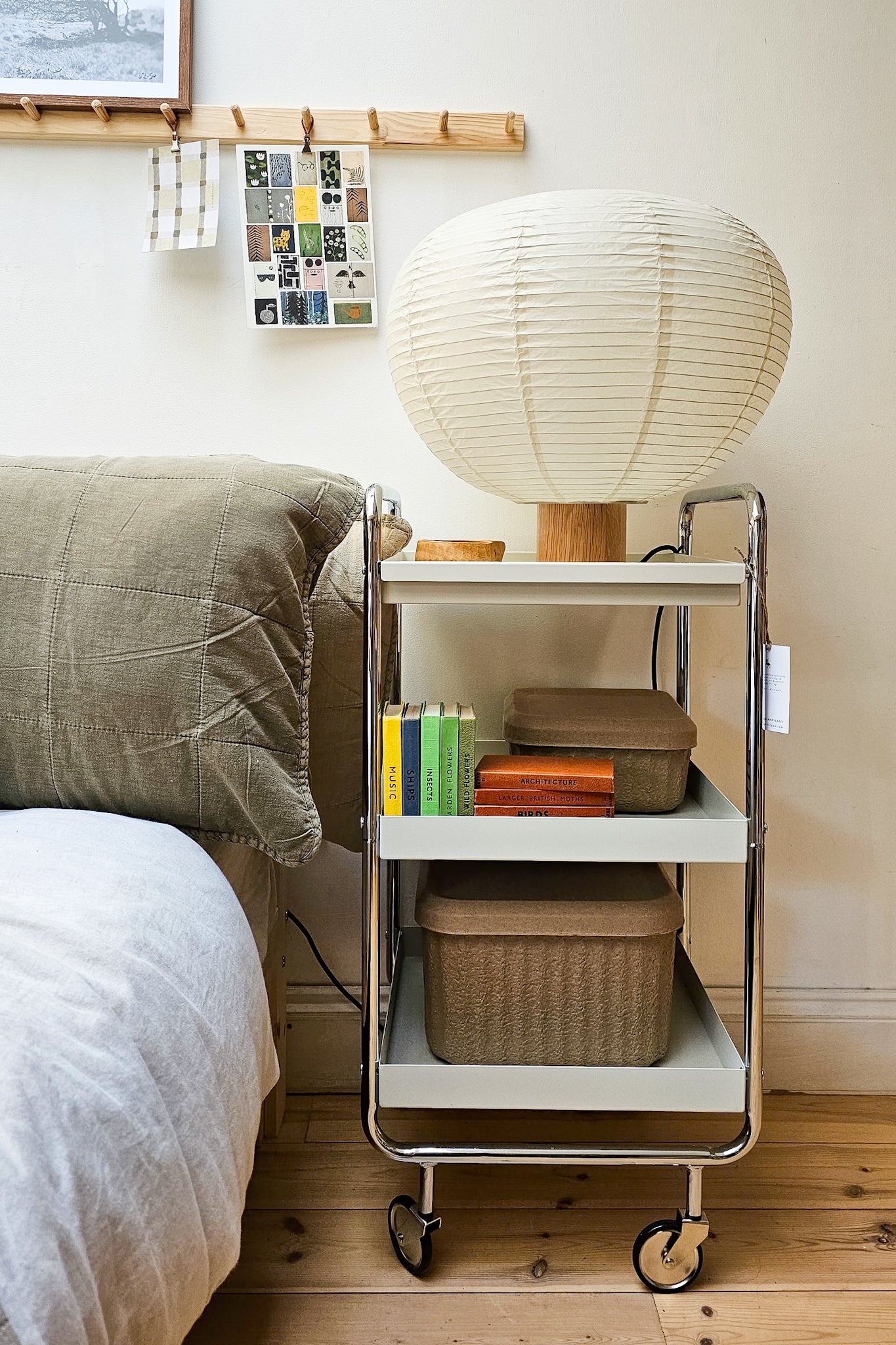 Collection of vintage Observer books styled on a three-tier trolley beside a bed, with Blomus storage boxes and a paper lantern lamp