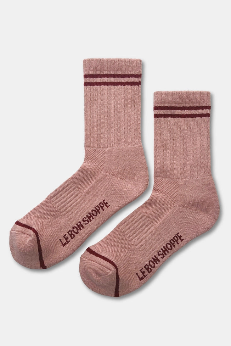 A pair of dusty pink crew socks with dark burgundy stripes near the cuffs and toes, featuring the brand name 'LE BON SHOPPE' printed in dark burgundy on the soles, shown against a light gray background.