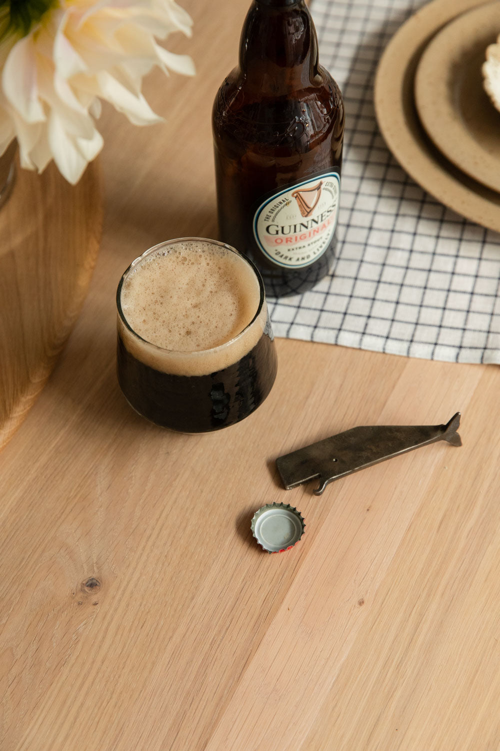 Whale bottle opener and bottle cap beside a glass of stout on an oak table
