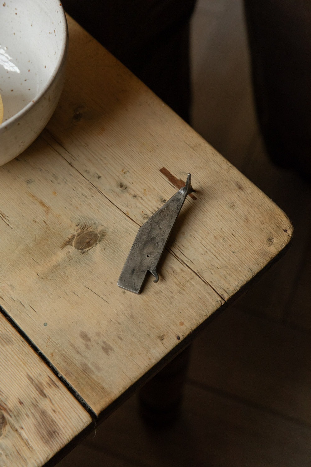 Whale-shaped metal bottle opener on the corner of a worn pine table