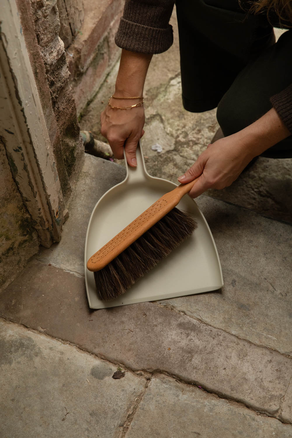 Hands sweeping a flagstone floor with a chalk white dustpan and brush
