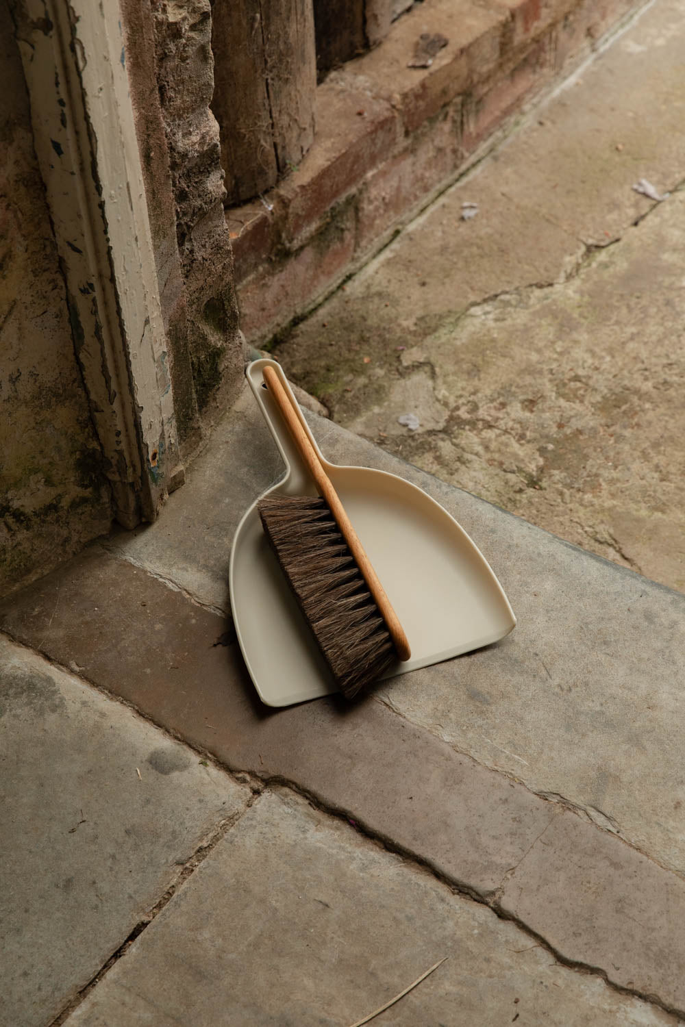 Chalk white dustpan with a wooden brush on a stone floor