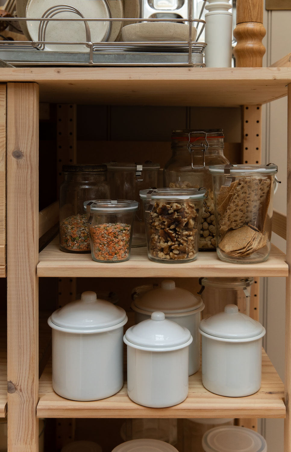 White enamel canisters and glass storage jars on simple pine pantry shelves