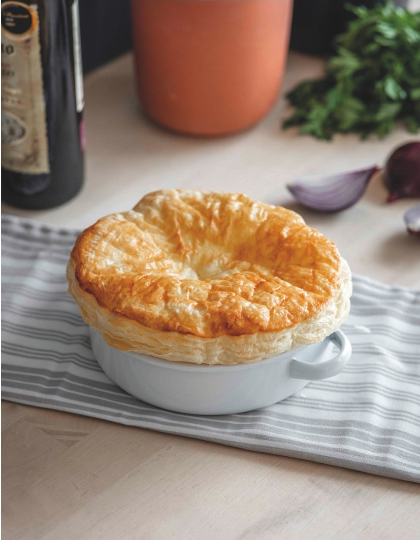 A filled white enamel pie dish with two handles, placed on a tea towel on a wooden surface.