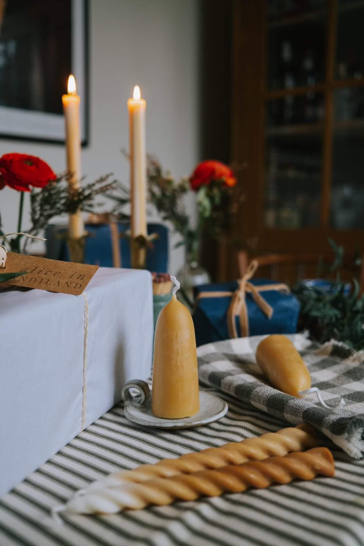 Christmas table with a checked cloth, red flowers and beeswax candles on ceramic candle plates
