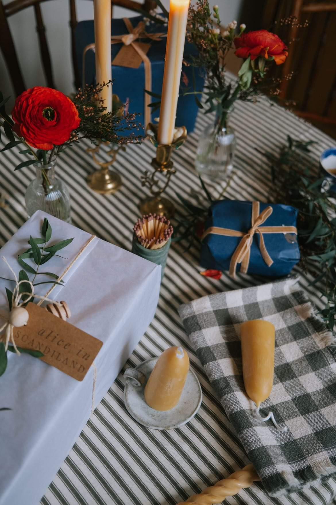 Festive table with beeswax candles on ceramic candle plates, wrapped presents and red flowers