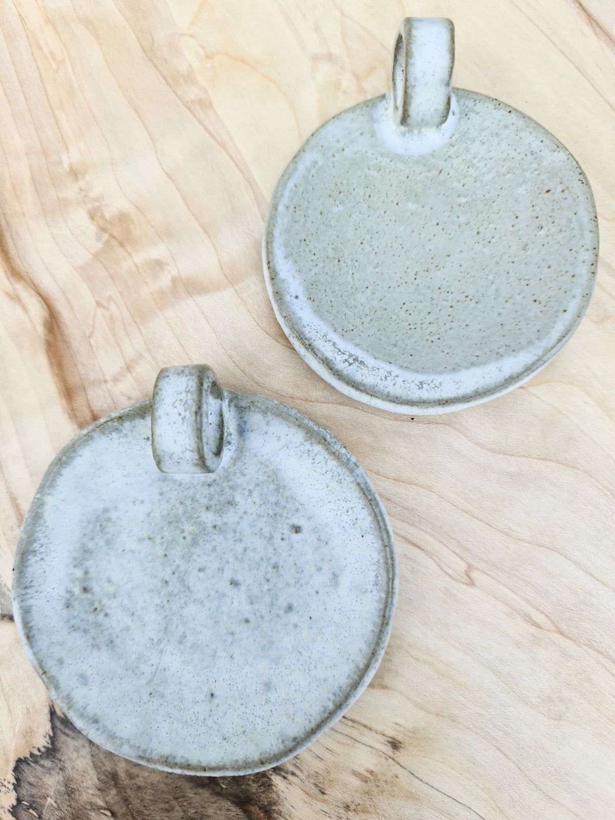 Two handmade ceramic candle plates from above, showing the speckled glaze and loop handles