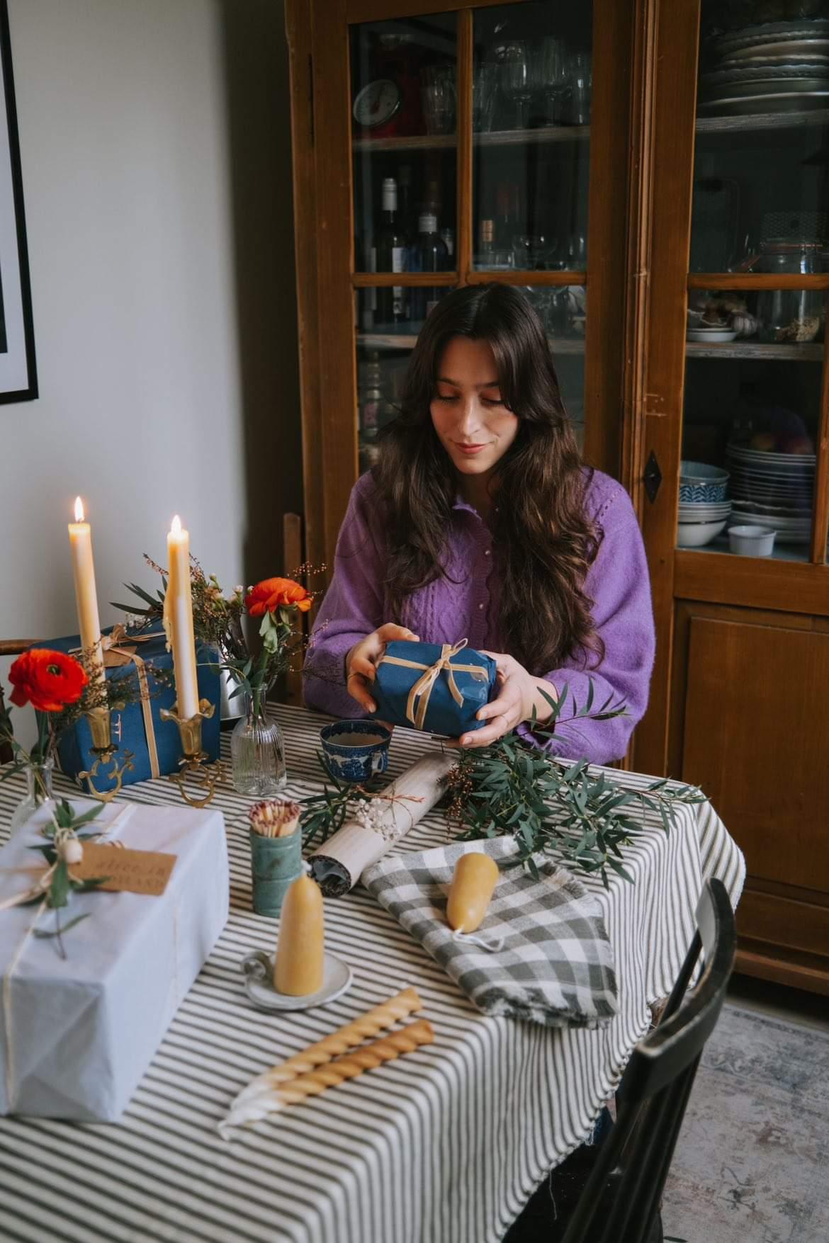 Setting a festive table with beeswax candles on ceramic plates, greenery and red flowers
