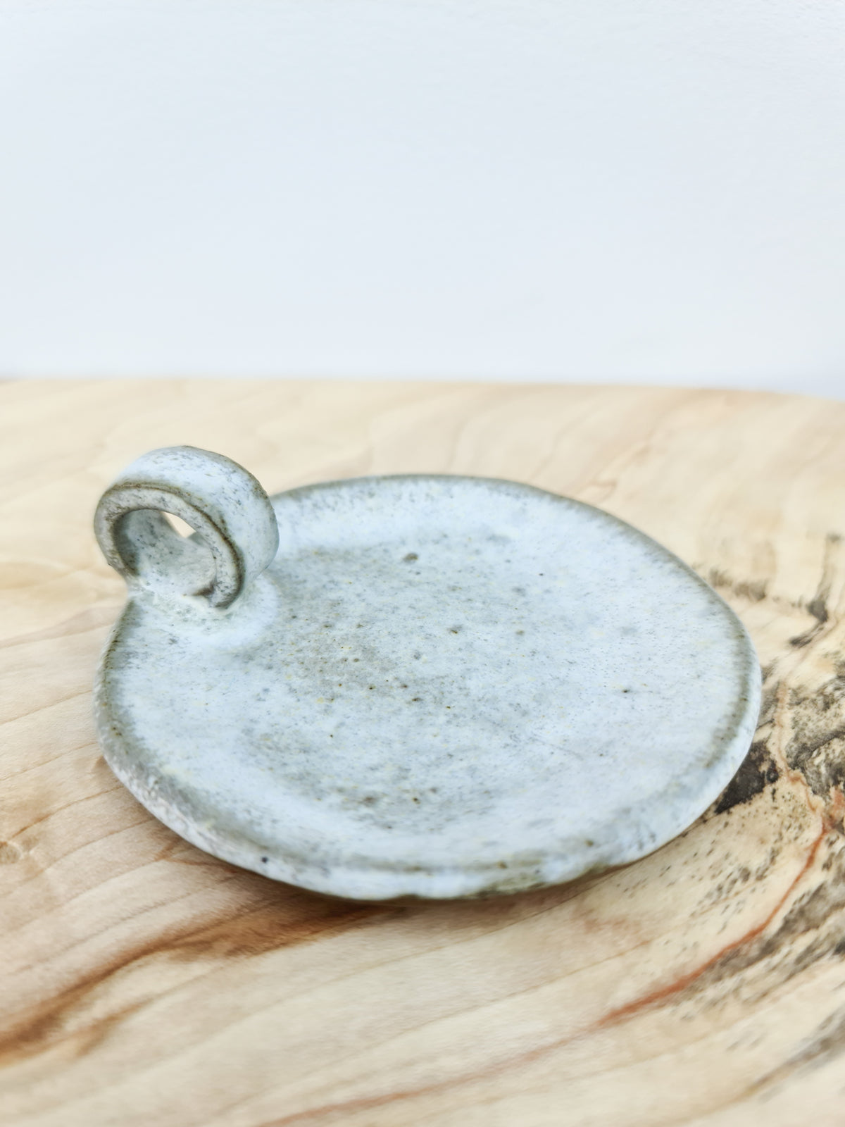 Side view of a handmade ceramic candle plate with a small loop handle