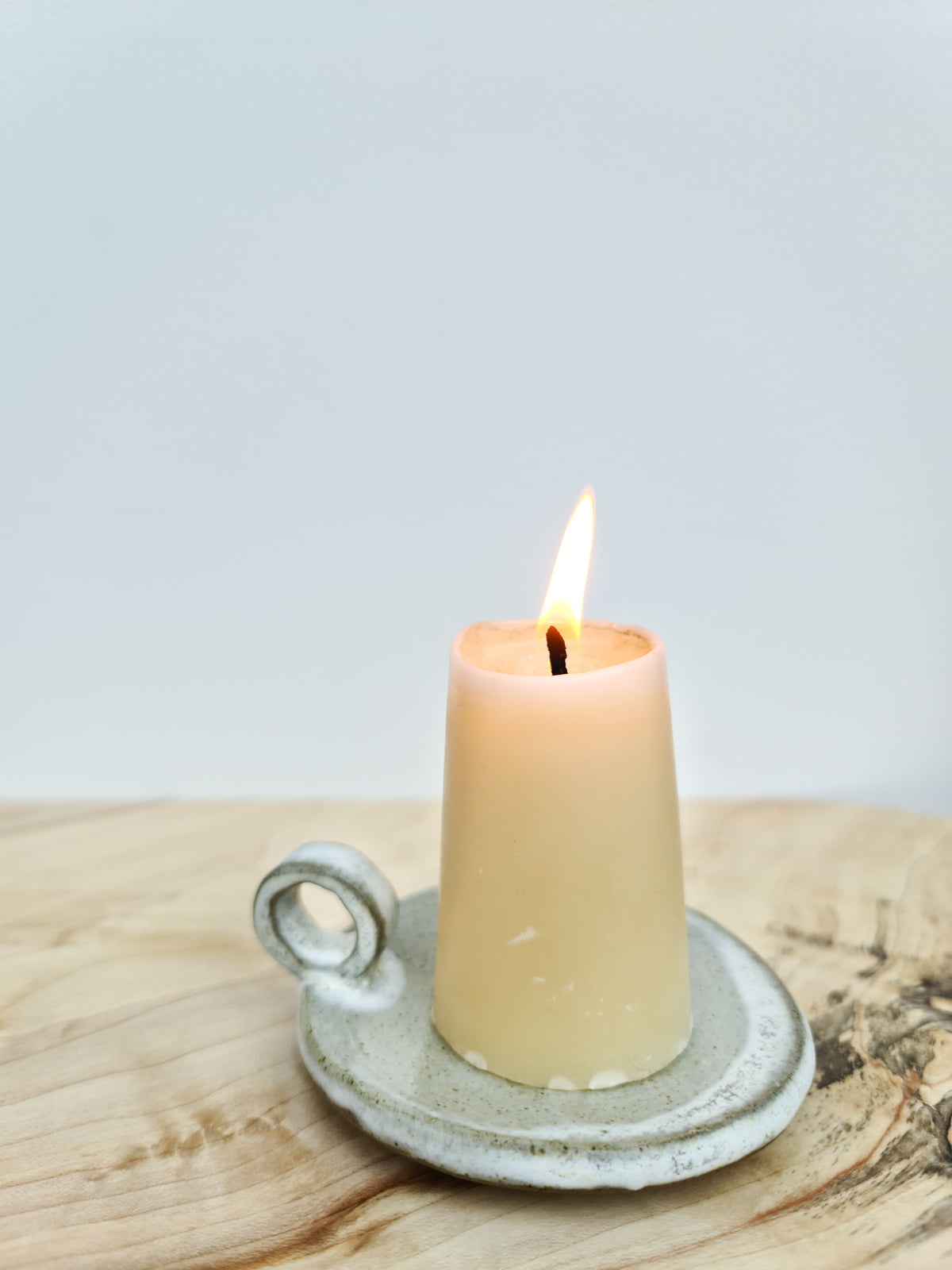 Lit beeswax Stumpie candle on a speckled white ceramic candle plate with a loop handle