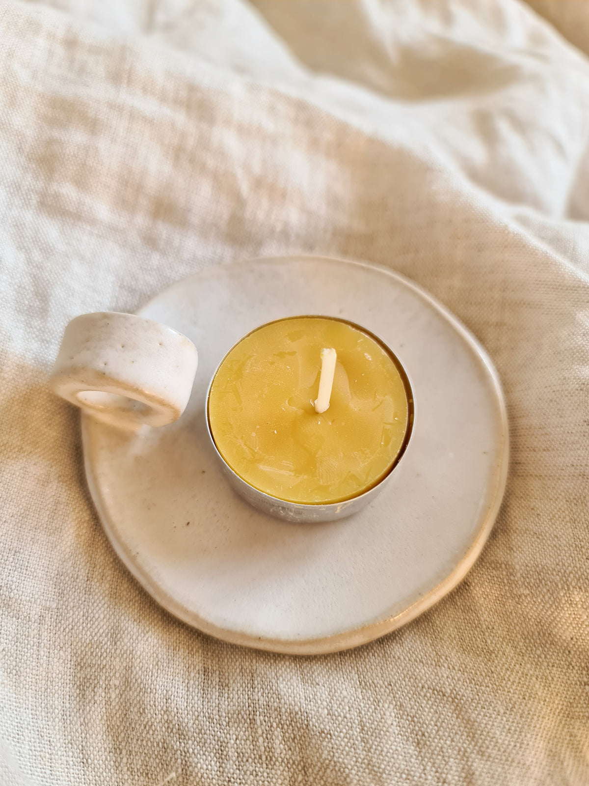 Beeswax tealight on a handmade ceramic candle plate on linen