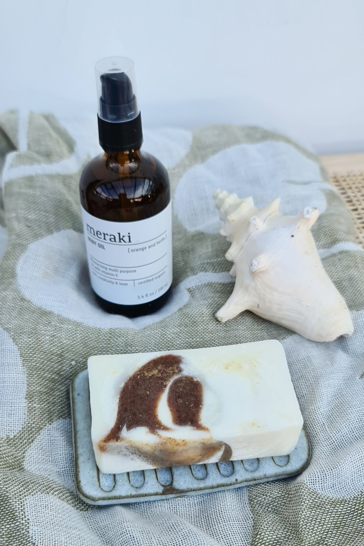 Bar of soap on a rustic ceramic soap dish beside an amber glass bottle and a shell