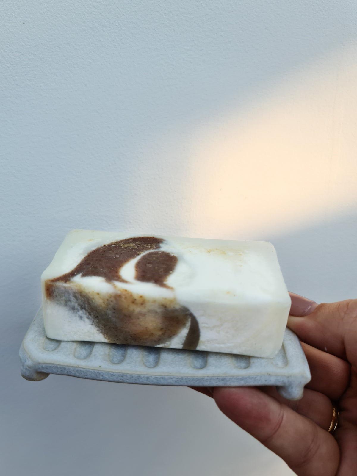 Hand holding a bar of soap on a rustic ceramic soap dish