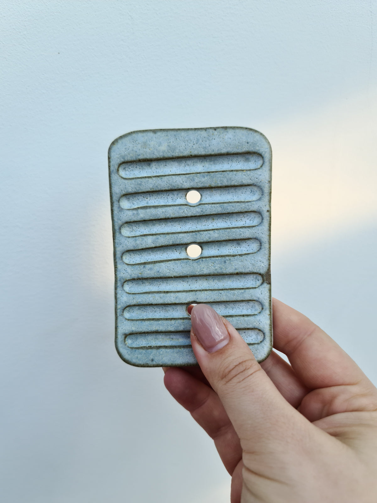 Hand holding a large rustic ceramic soap dish showing the ridges and drainage holes