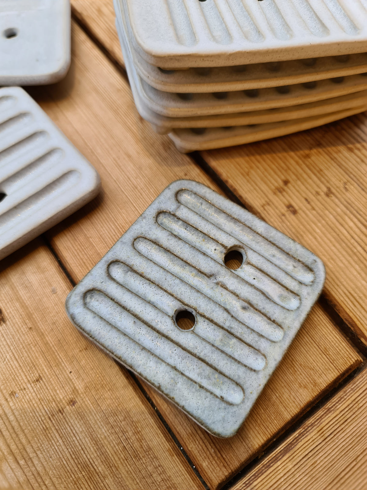 Rustic ceramic soap dish with ridges and drainage holes beside a stack of dishes