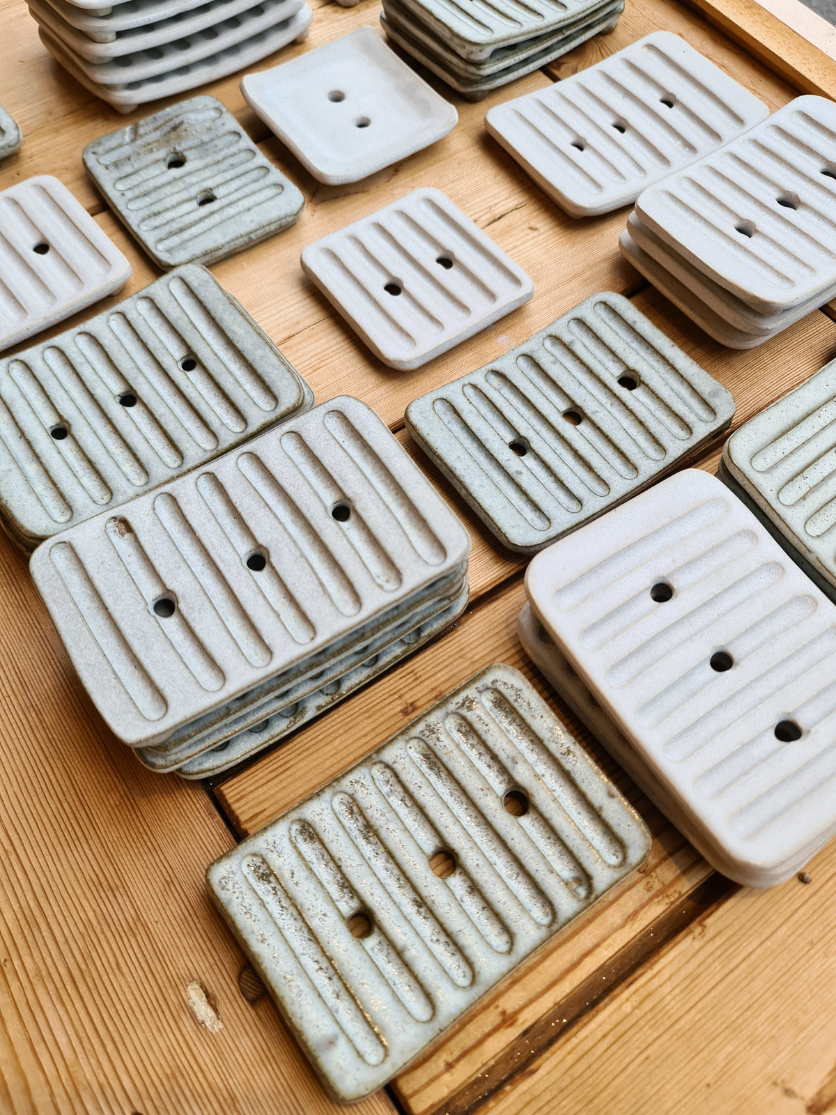 Collection of handmade white and rustic ceramic soap dishes on wooden boards