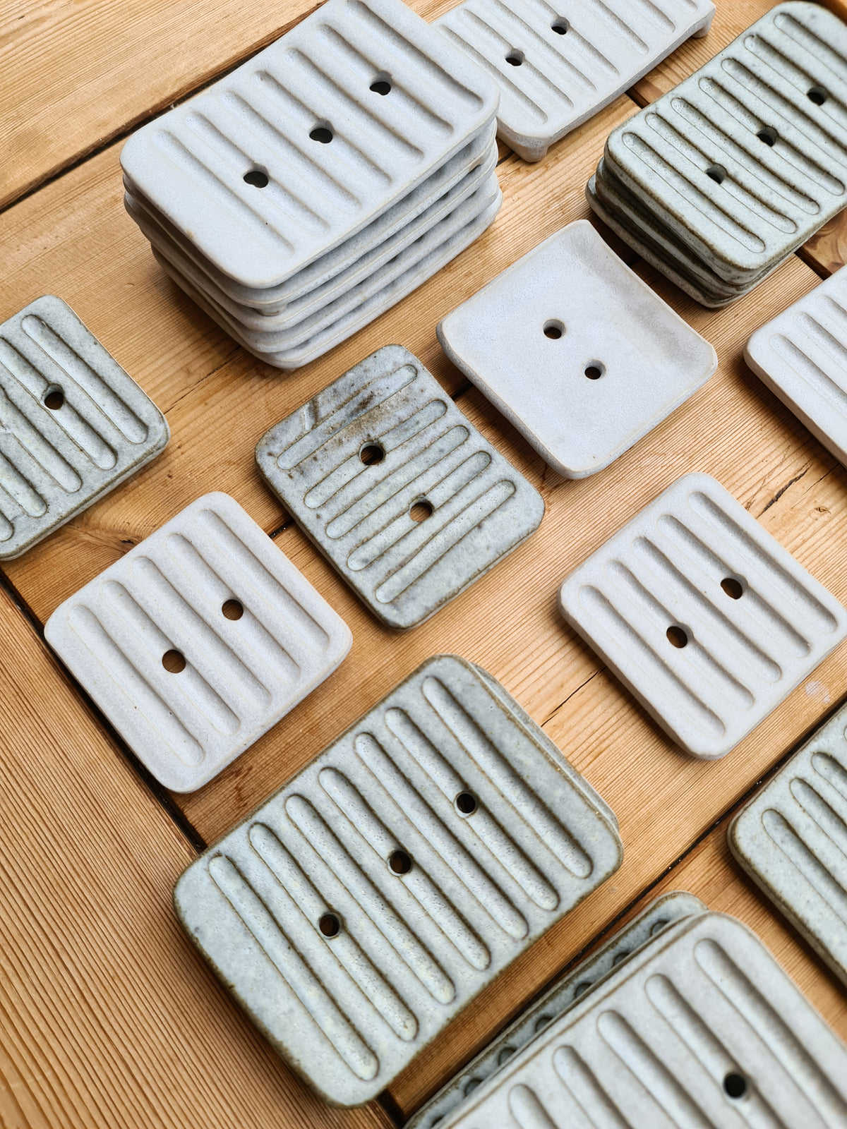 White and rustic handmade ceramic soap dishes laid out on a wooden table